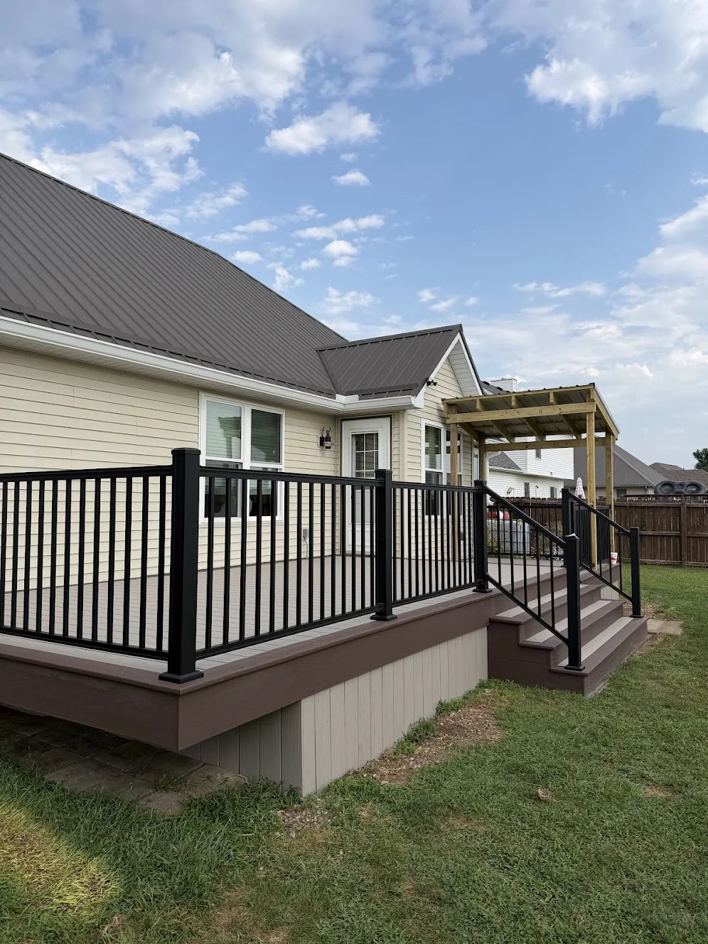 Composite deck with black railings, wide steps and a timber pergola beside a home.
